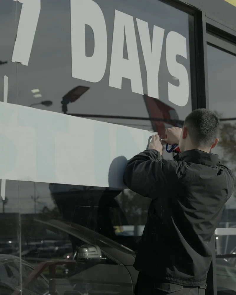 Installer positioning large vinyl lettering on a car dealership window