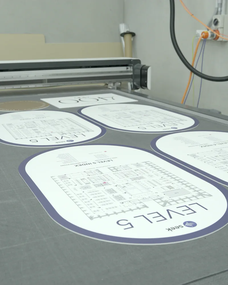 Printed floor-plan directory signs for Seek laid out on a flatbed cutting table