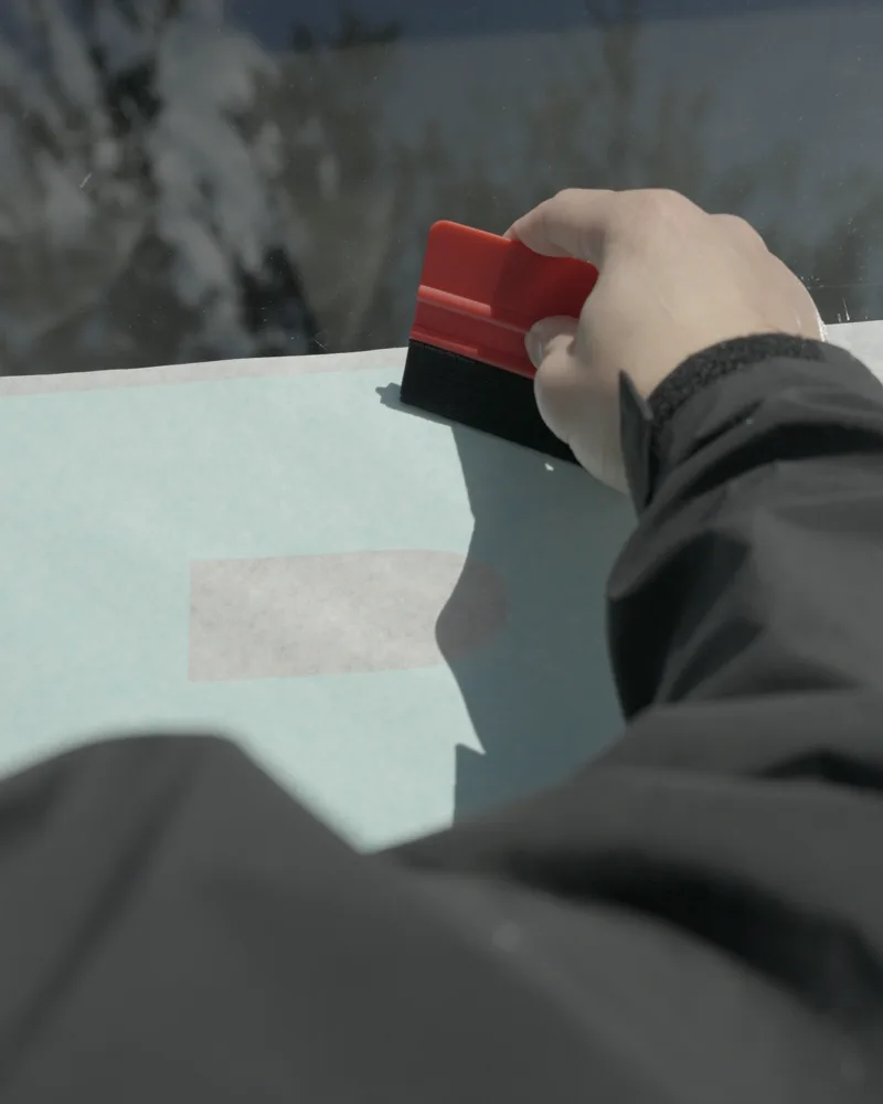 Installer pressing cut vinyl window lettering onto glass with a red squeegee